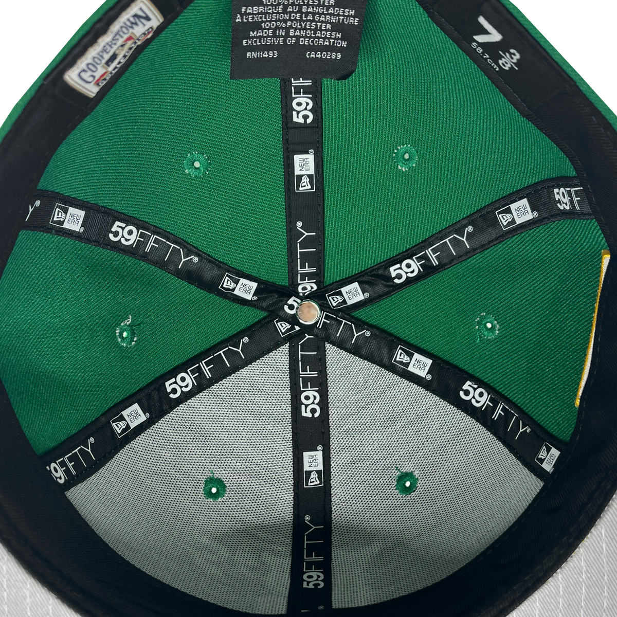 The image shows the inside of a New Era Oakland Ballers 59Fifty Cap, likely worn by an Oakland Ballers fan. The interior includes black lining adorned with repeated white "59FIFTY" text and logos. Visible tags provide details on size, manufacturing, and materials in English, Spanish, and French. The cap is size 7 3/8.